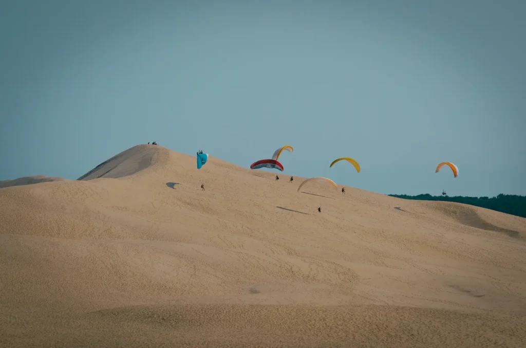 tir-longue-distance-parapentes-atterrissant-dune-sable-ciel-bleu-clair